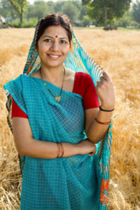 Home portrait of happy indian woman standing in agricultural field